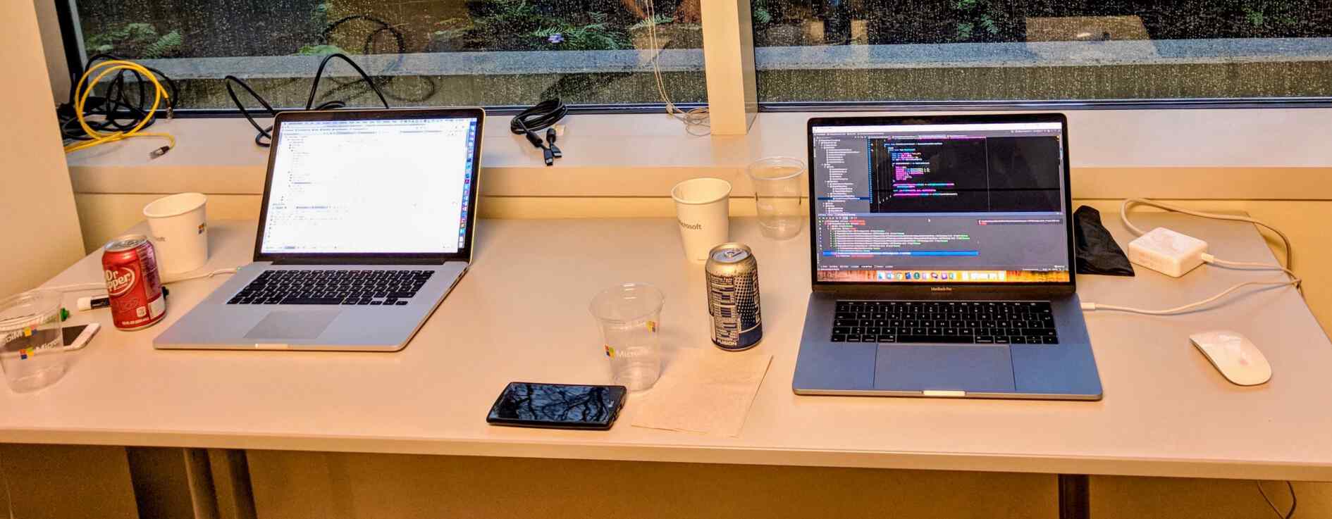 Aufnahme von zwei Laptops an einem Tisch am Fenster mit Code auf dem Screen